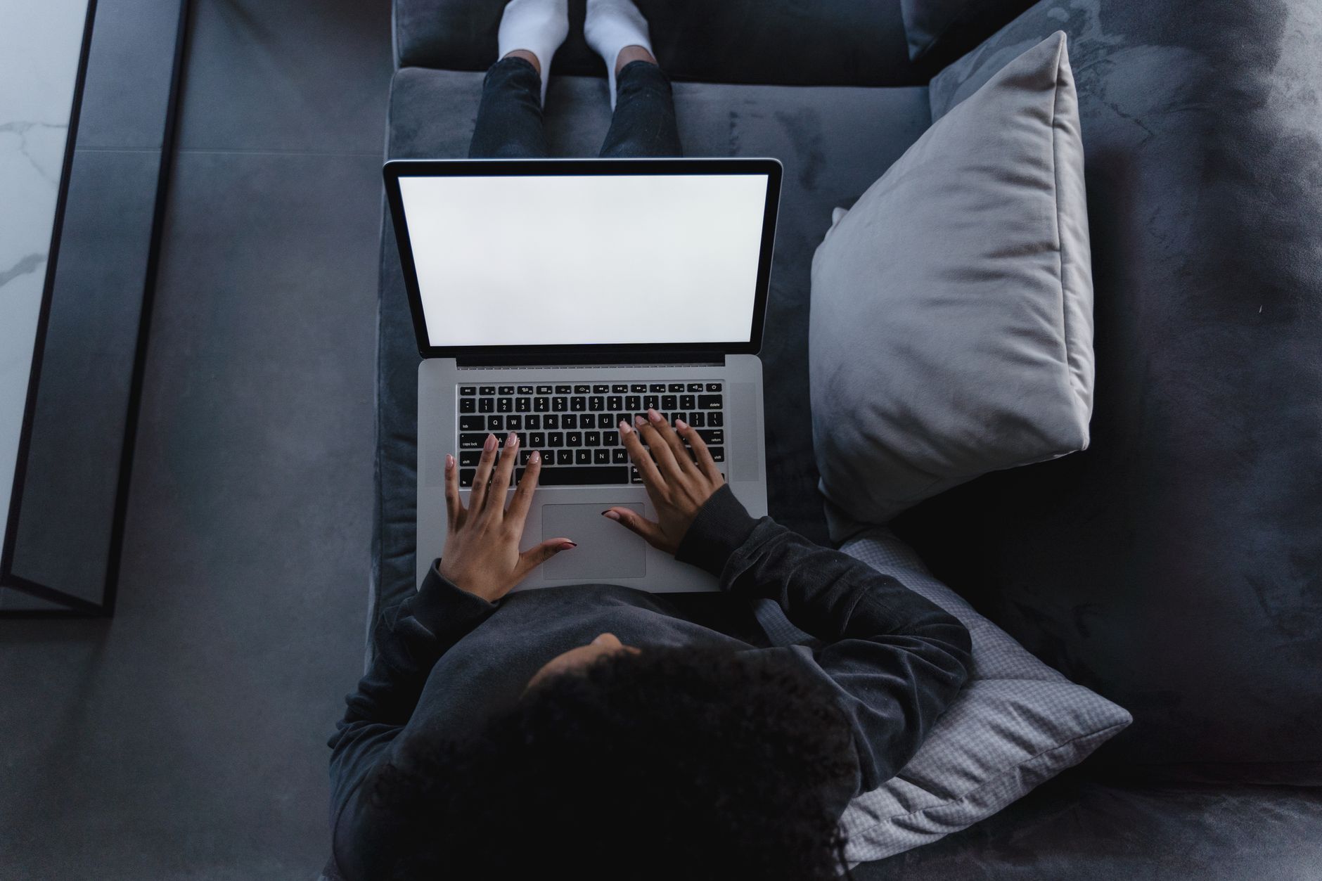En person sidder afslappet i en sofa og bruger en bærbar computer, set ovenfra.