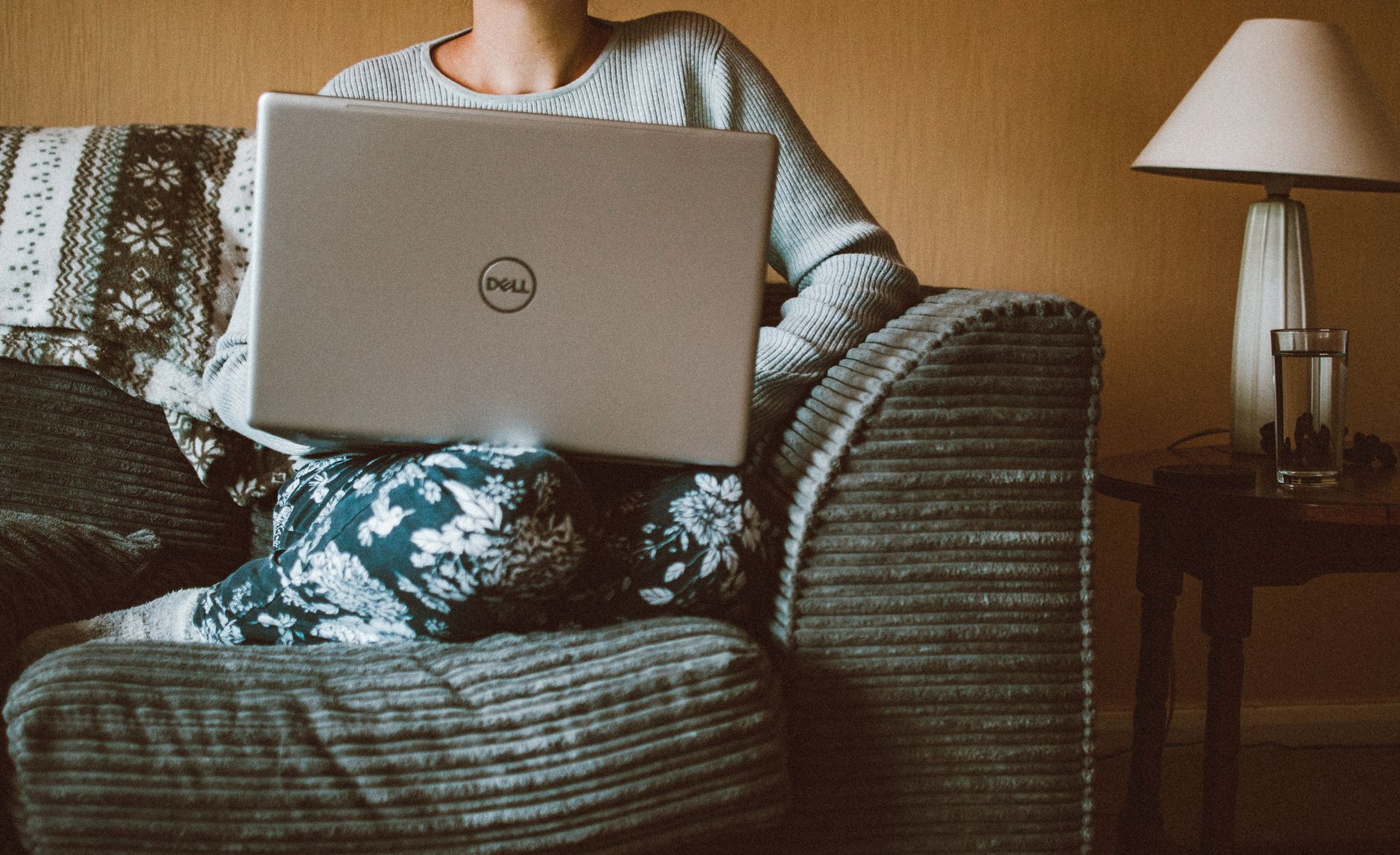 En kvinde i afslappet tøj arbejder på en bærbar computer, mens hun sidder i en hyggelig sofa indendørs.